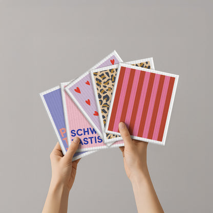 Naturfaser-Schwammtuch mit roten und rosafarbenen Streifen, zwischen weiteren Tüchern gehalten
