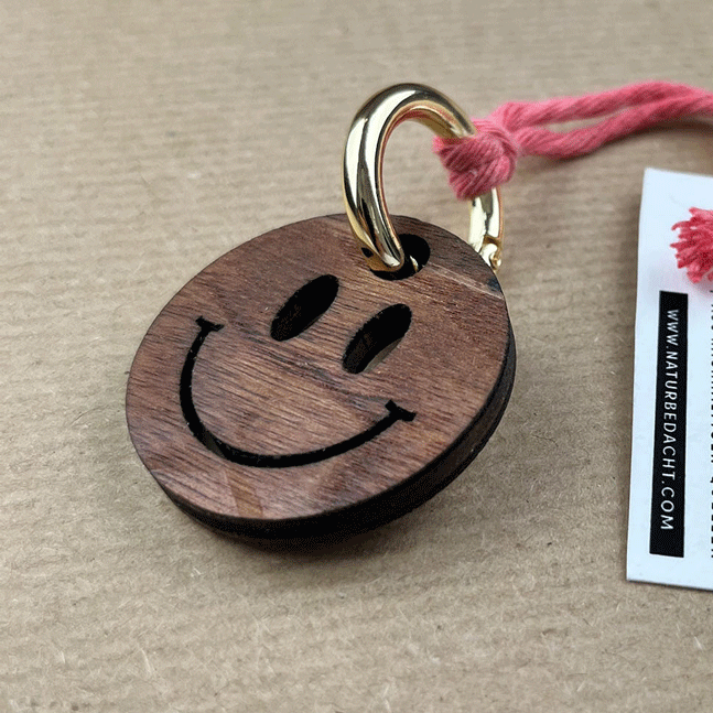 Schlüsselanhänger Smiley aus dunkelbraunem Holz mit Metallkarabiner und pinkem Band